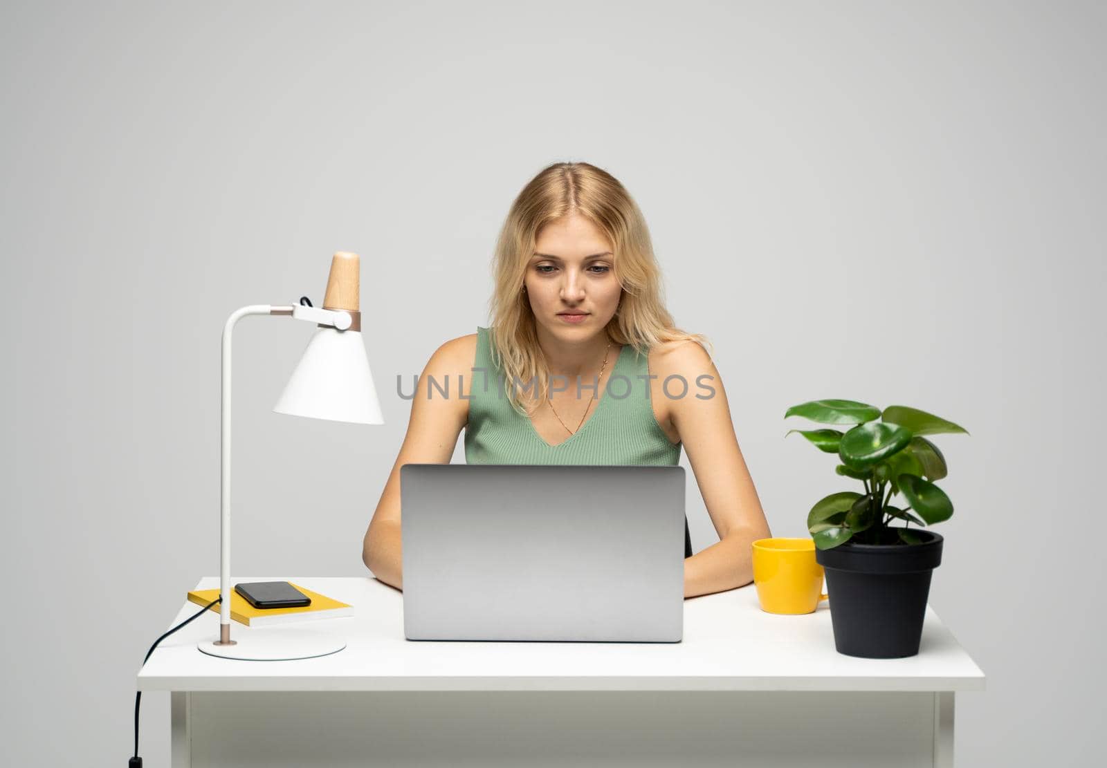 Portrait of a pretty young woman studying while sitting at the table with grey laptop computer, notebook. Smiling business woman working with a laptop isolated on a grey background. by vovsht