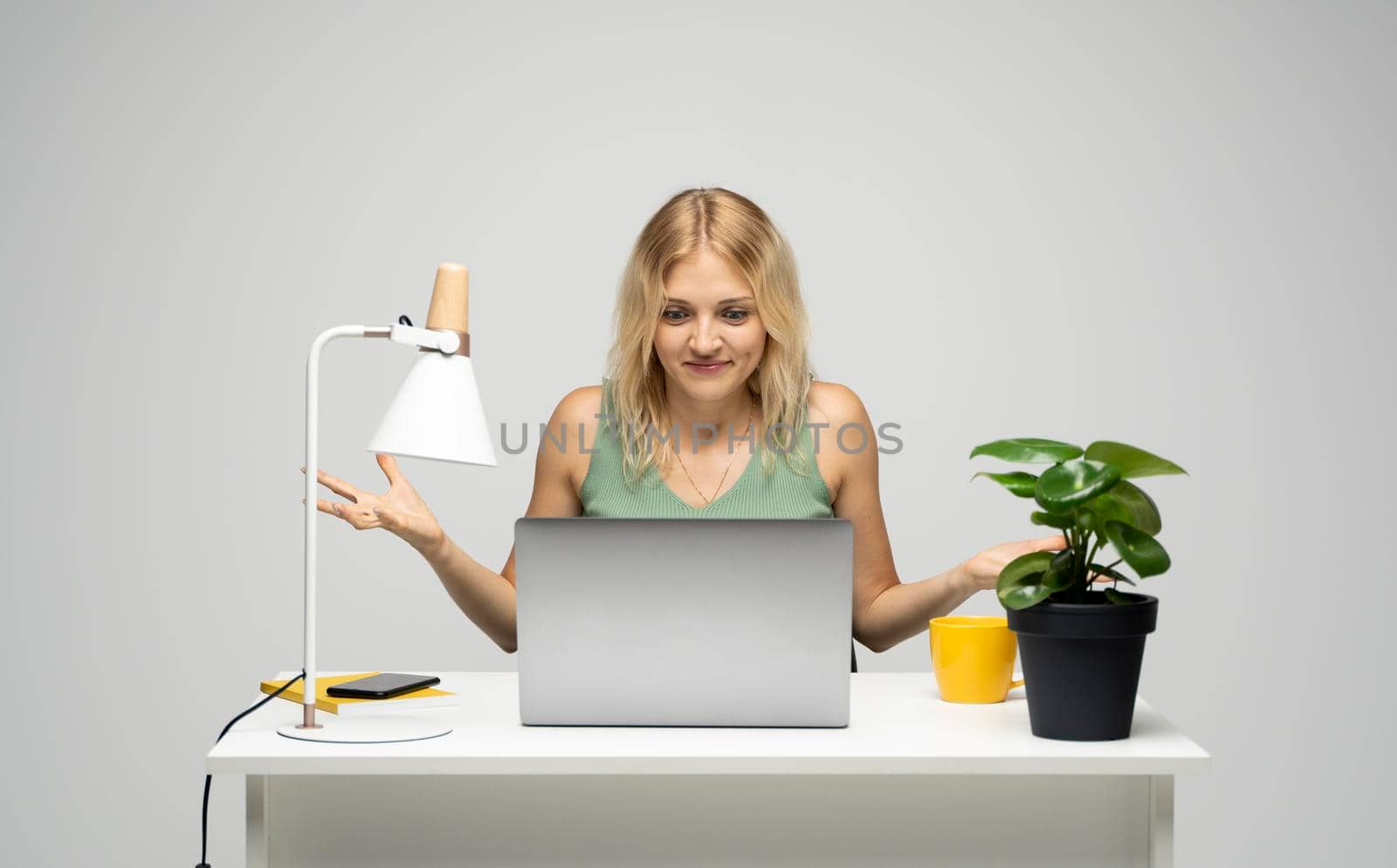 Confused young attractive business woman or student with a blond hair sitting at the table and working on a laptop. Young cheerful student girl . Studying