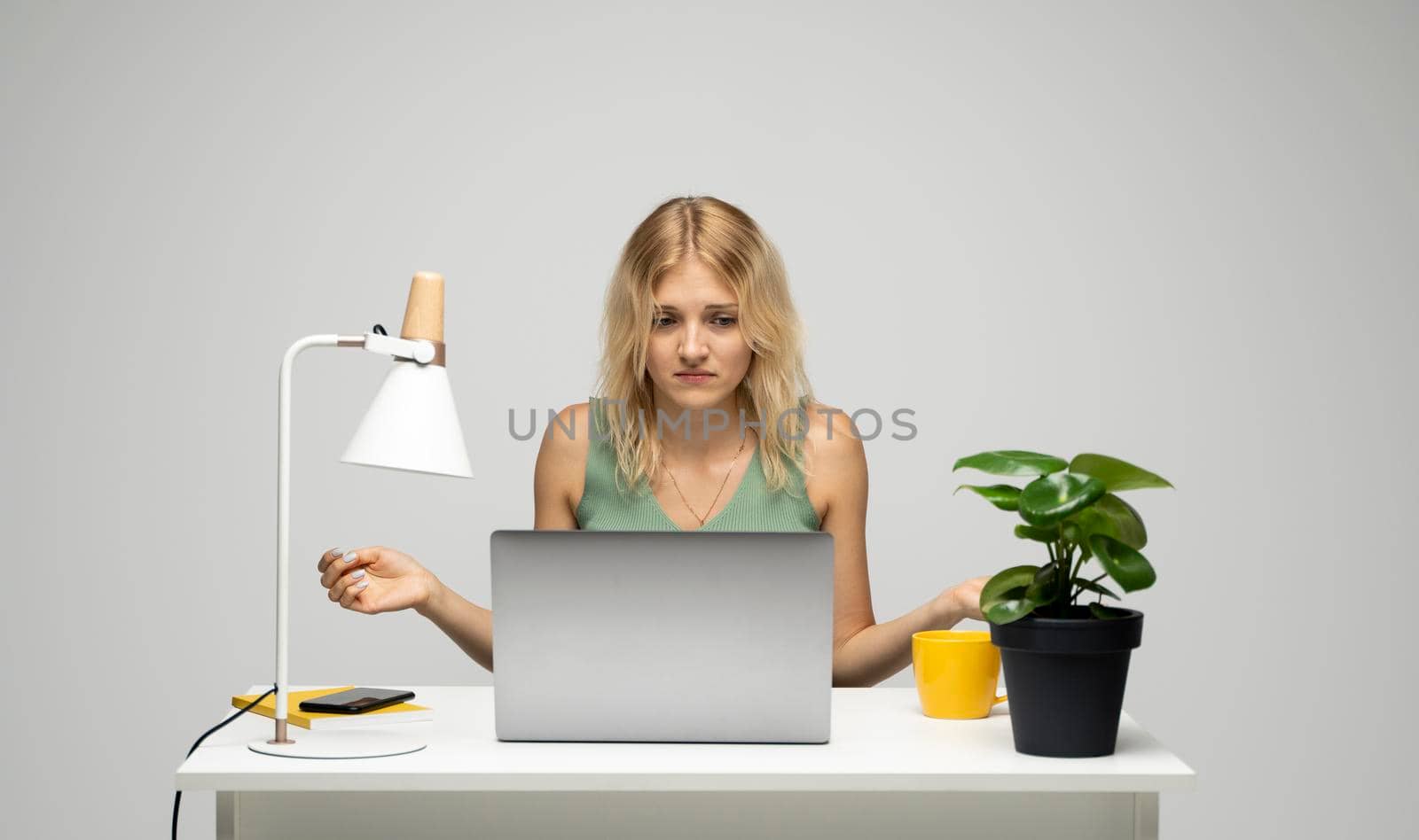 Confused blonde business woman working on a laptop on a white background. by vovsht