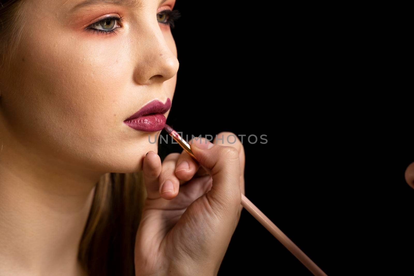 Makeup artist applies red lipstick on a beautiful woman face. Hand of make-up master, painting lips of young beauty model girl. Make up in process