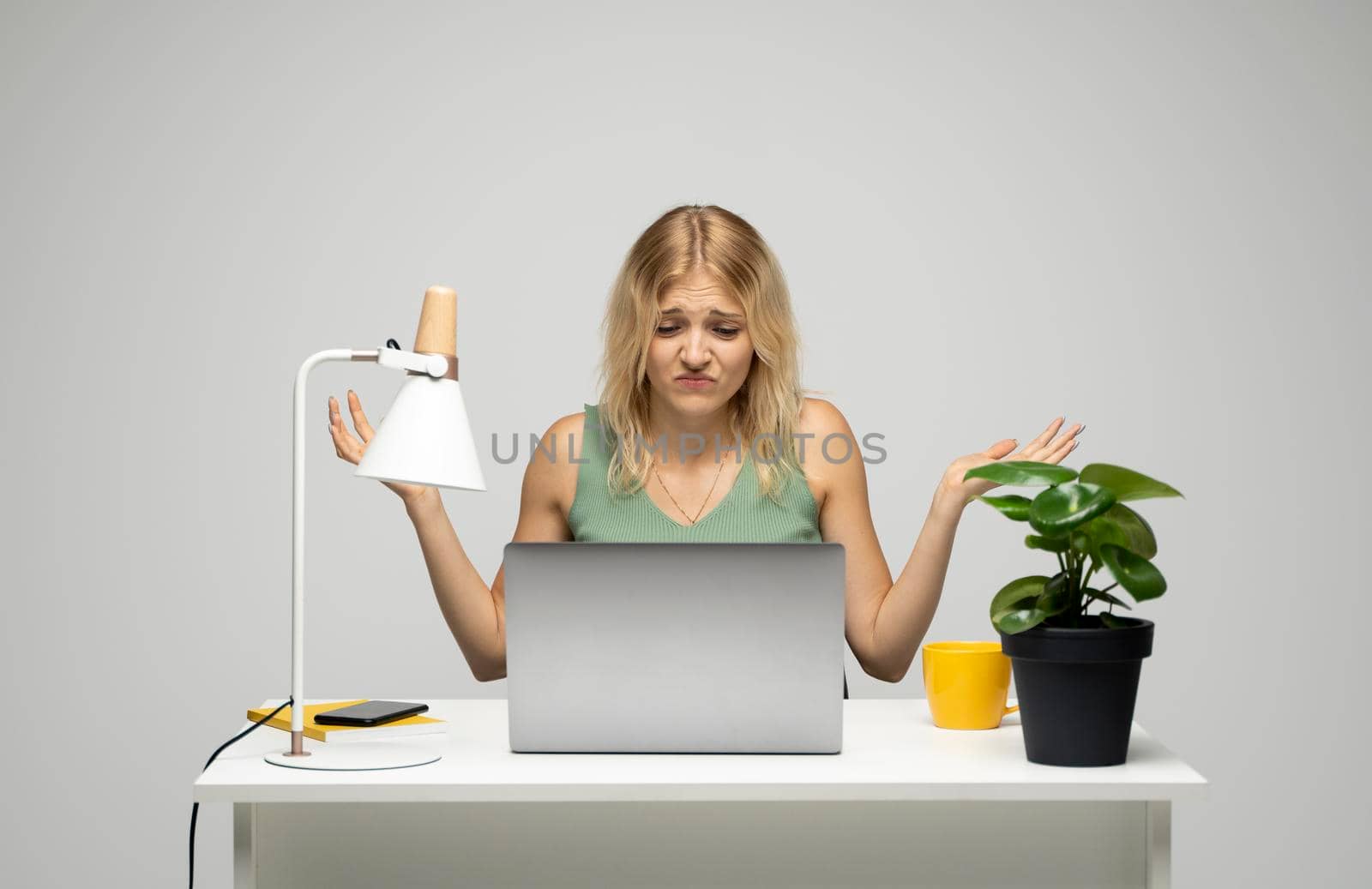 Confused designer woman in a green t-shirt looking at her laptop in a bright creative office. Business and education concept. by vovsht