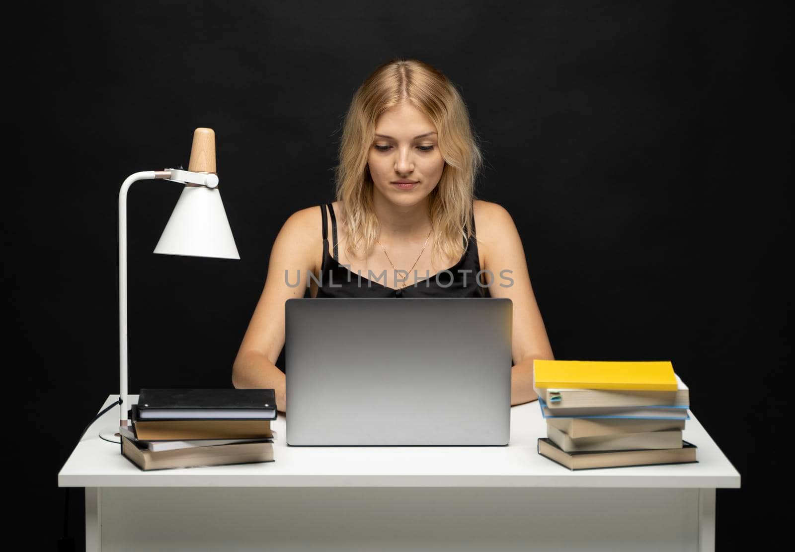 Portrait of a pretty young woman studying while sitting at the table with grey laptop computer, notebook. Smiling business woman working with a laptop isolated on a grey background. by vovsht