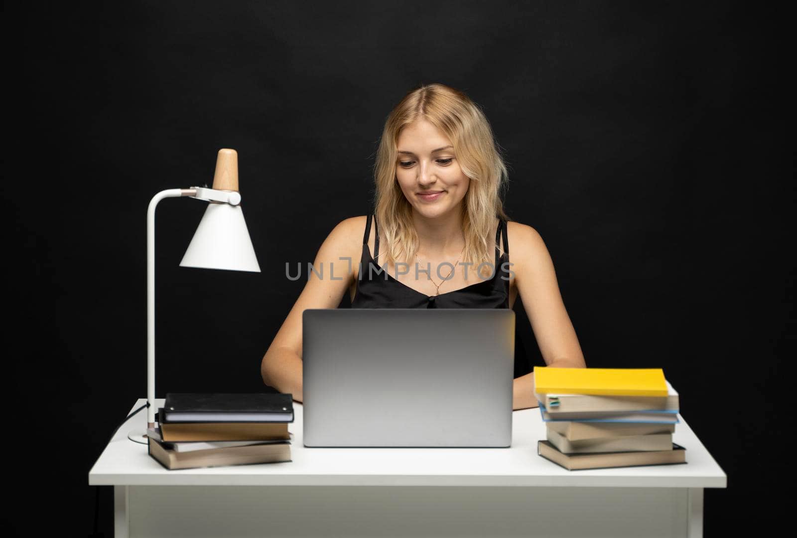 Portrait of a pretty young woman studying while sitting at the table with grey laptop computer, notebook. Smiling business woman working with a laptop isolated on a grey background. by vovsht