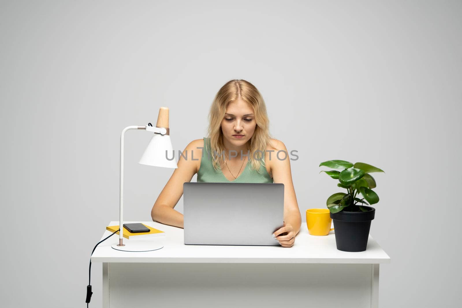 Portrait of a pretty young woman studying while sitting at the table with grey laptop computer, notebook. Smiling business woman working with a laptop isolated on a grey background