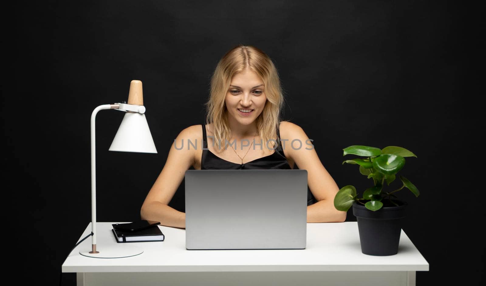 Portrait of a pretty young woman studying while sitting at the table with grey laptop computer, notebook. Smiling business woman working with a laptop isolated on a grey background