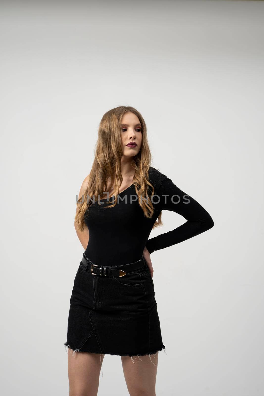 Beautiful young woman portrait in a black t-shirt and mini skirt. Studio shot, isolated on gray background. by vovsht