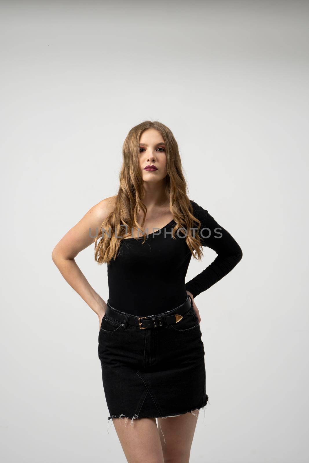 Beautiful young woman portrait in a black t-shirt and mini skirt. Studio shot, isolated on gray background. by vovsht