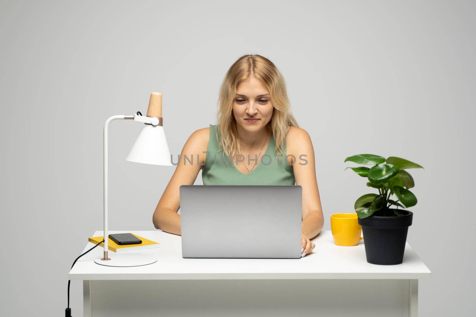 Portrait of a pretty young woman studying while sitting at the table with grey laptop computer, notebook. Smiling business woman working with a laptop isolated on a grey background. by vovsht