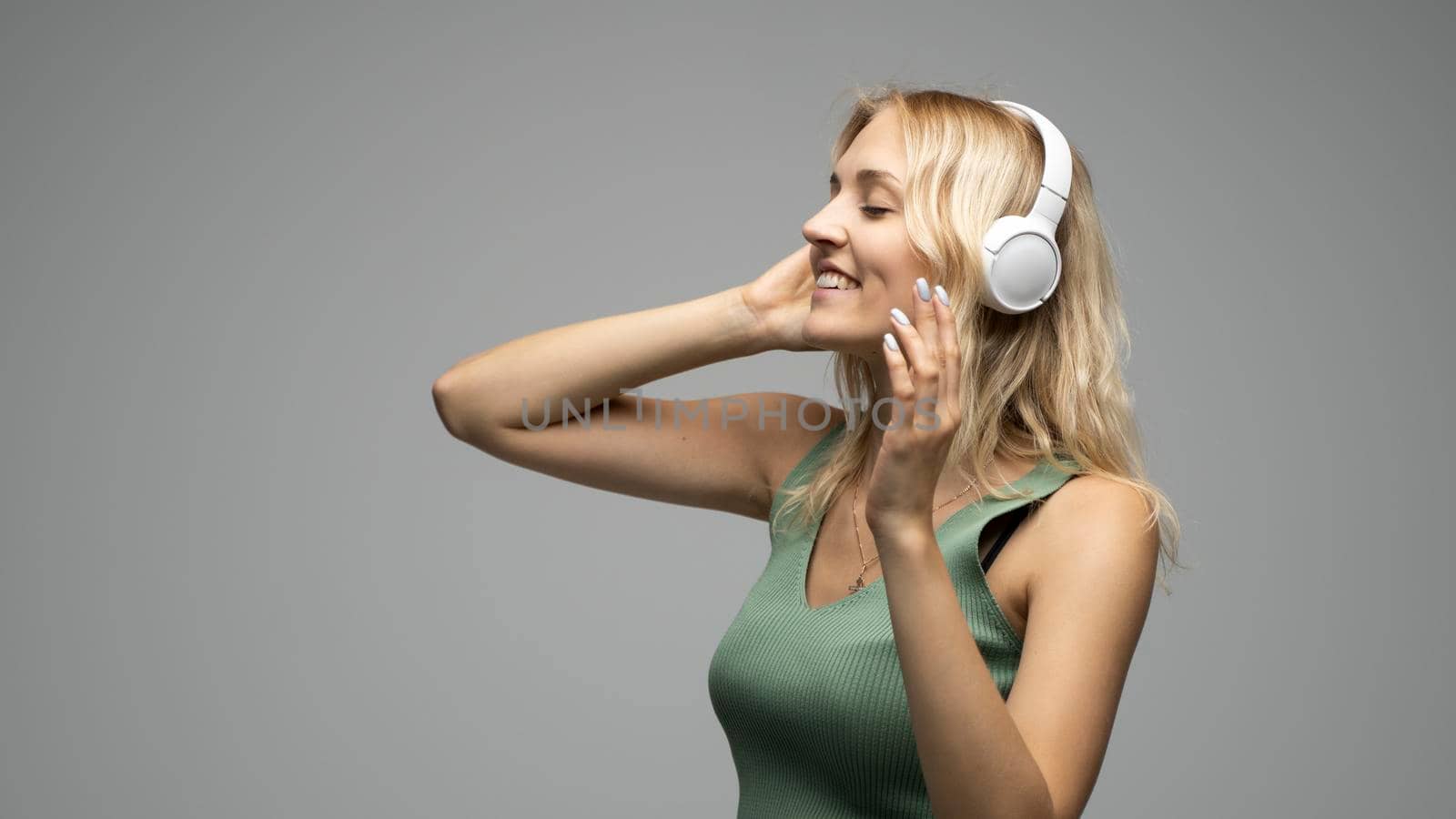 Beautiful young woman listening to music in headphones on grey background