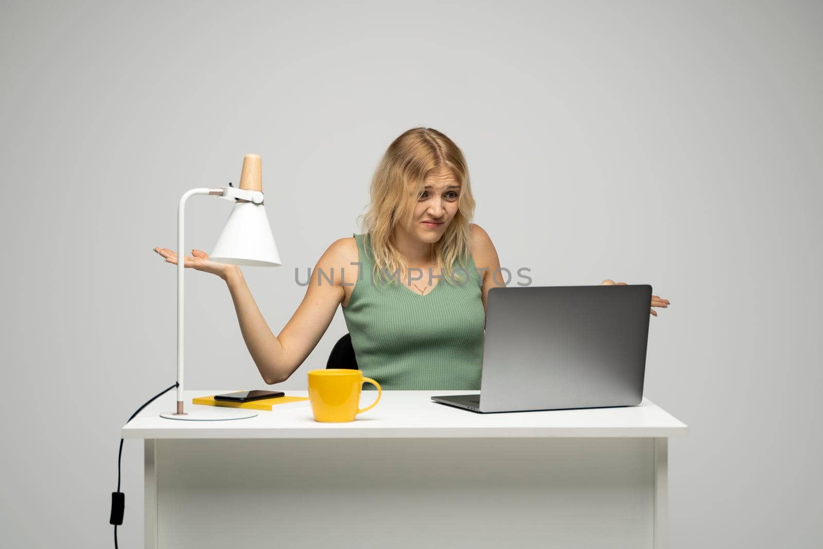 Confused designer woman in a green t-shirt looking at her laptop in a bright creative office. Business and education concept. by vovsht