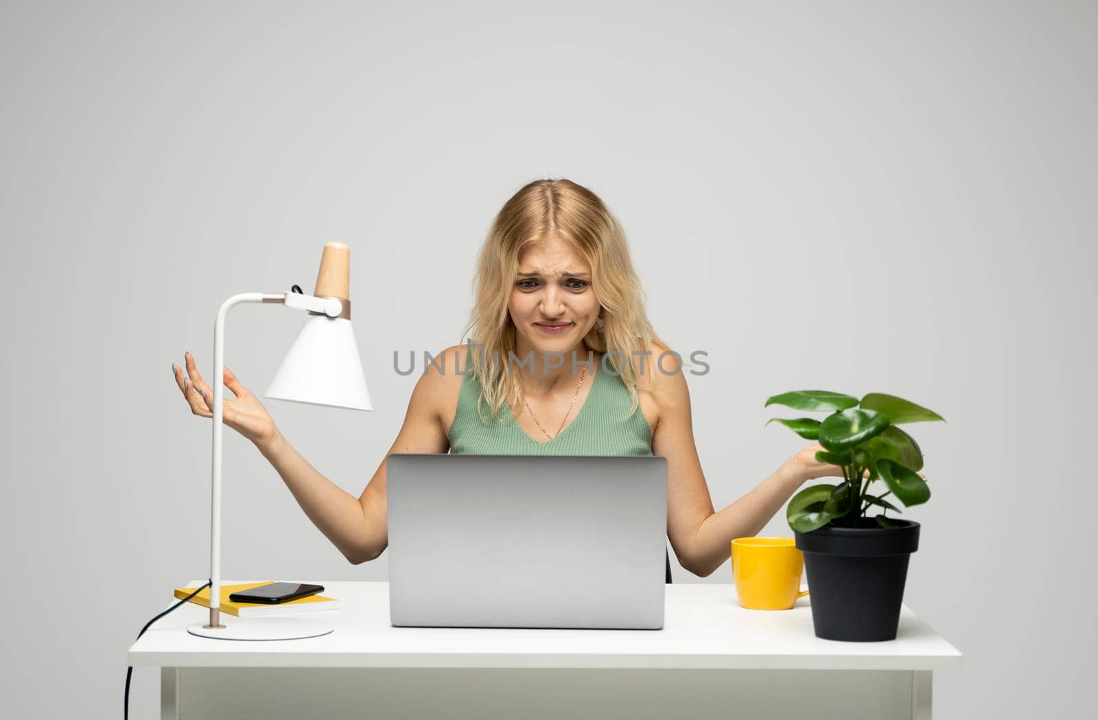 Confused designer woman in a green t-shirt looking at her laptop in a bright creative office. Business and education concept