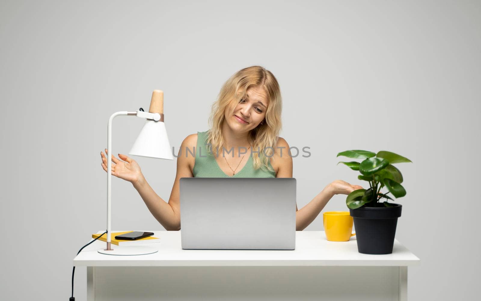 Confused young attractive business woman or student with a blond hair sitting at the table and working on a laptop. Young cheerful student girl . Studying