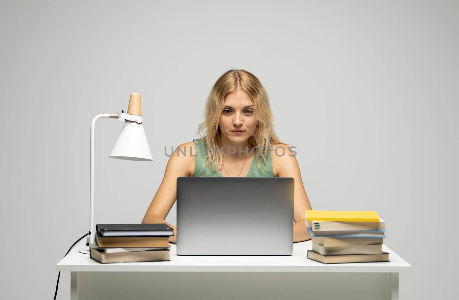 Smiling business woman working with a laptop isolated on a grey background. Portrait of a pretty young woman studying while sitting at the table with grey laptop computer, notebook. by vovsht