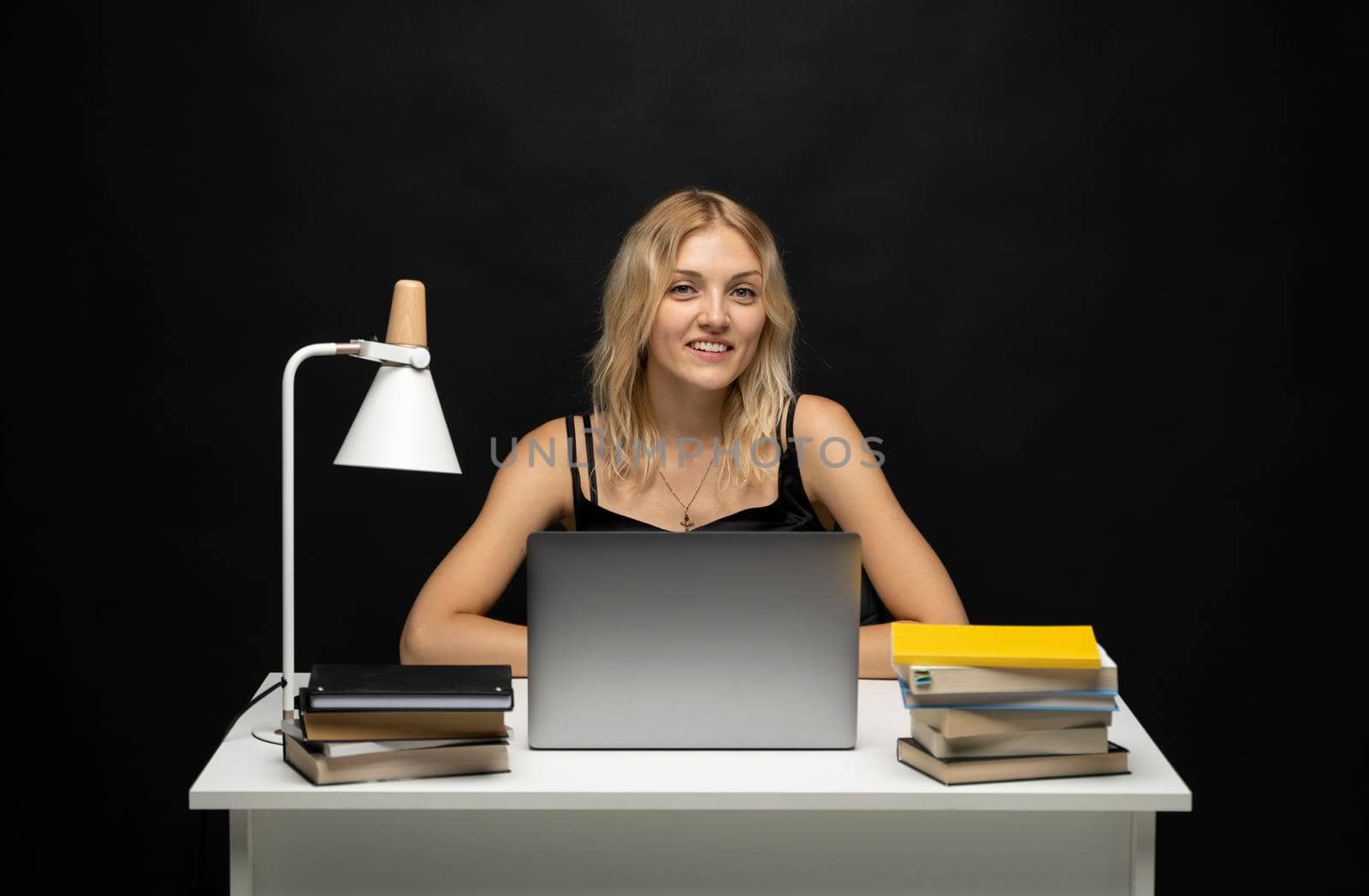 Portrait of Smiling pretty young woman studying while sitting at the table with grey laptop computer, notebook. Business woman working with a laptop isolated on a yellow background