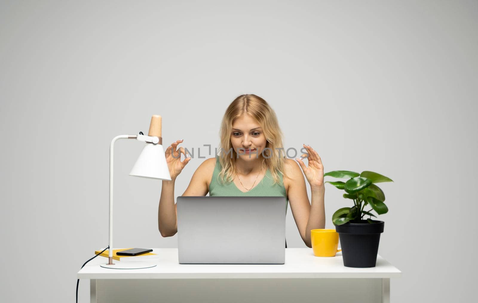 Picture of happy young lady chatting by laptop computer looking on a screen and showing okay gesture
