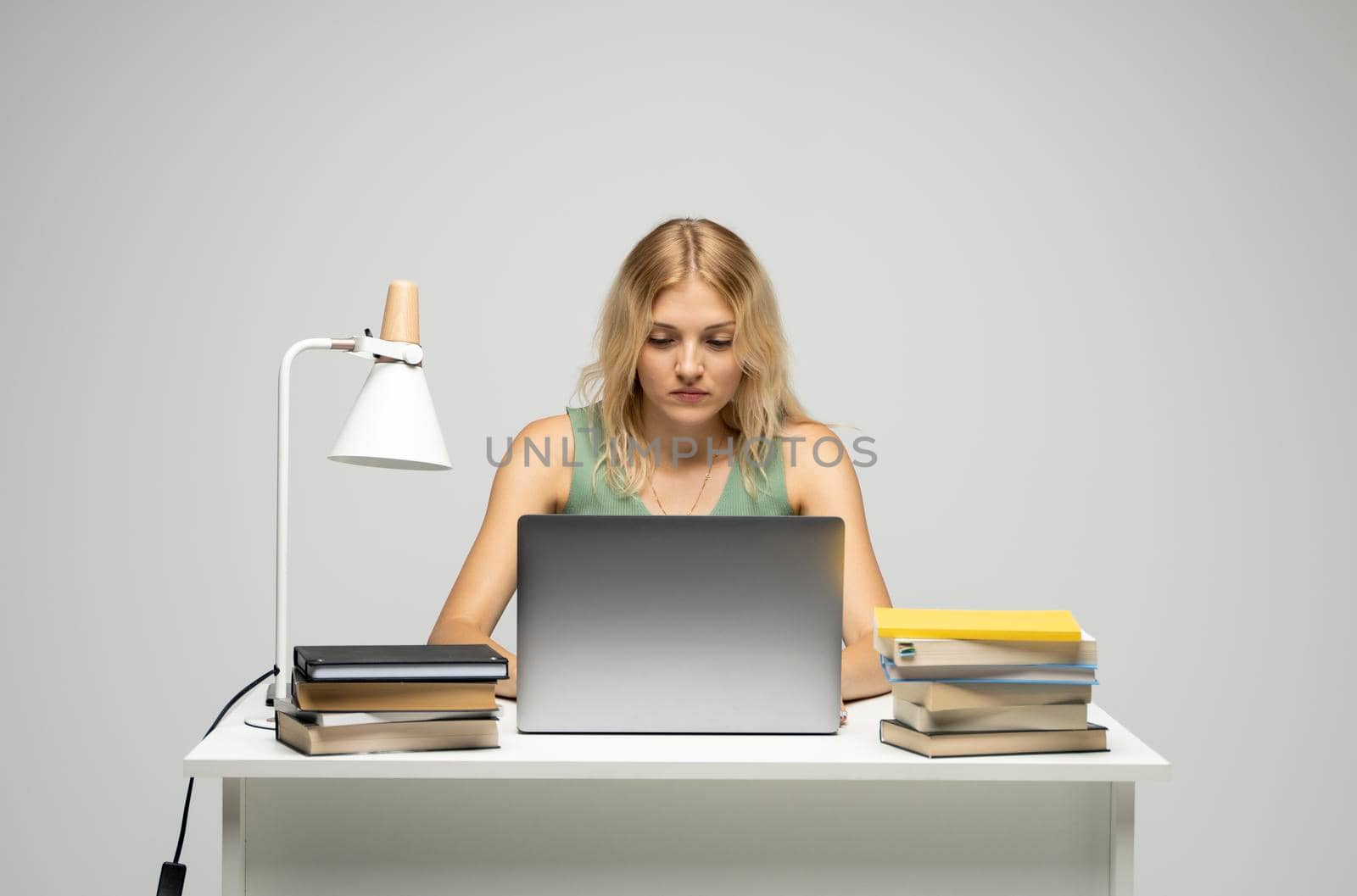 Portrait of a pretty young woman studying while sitting at the table with grey laptop computer, notebook. Smiling business woman working with a laptop isolated on a grey background