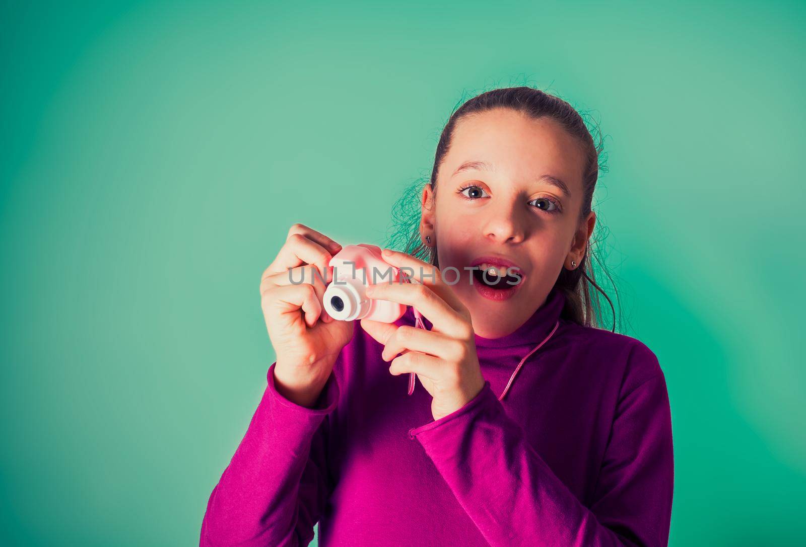 Little Girl Taking Picture Using Toy Photo Camera on cyan background