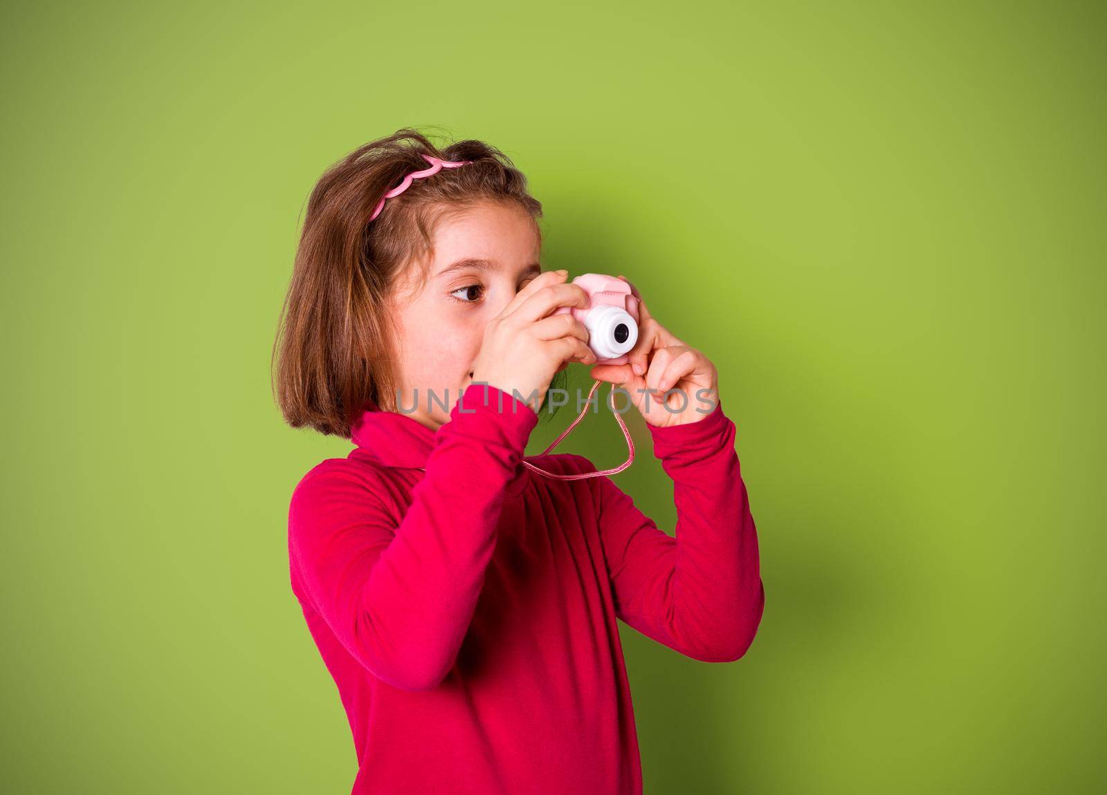 Little Girl Taking Picture Using Toy Photo Camera on green background