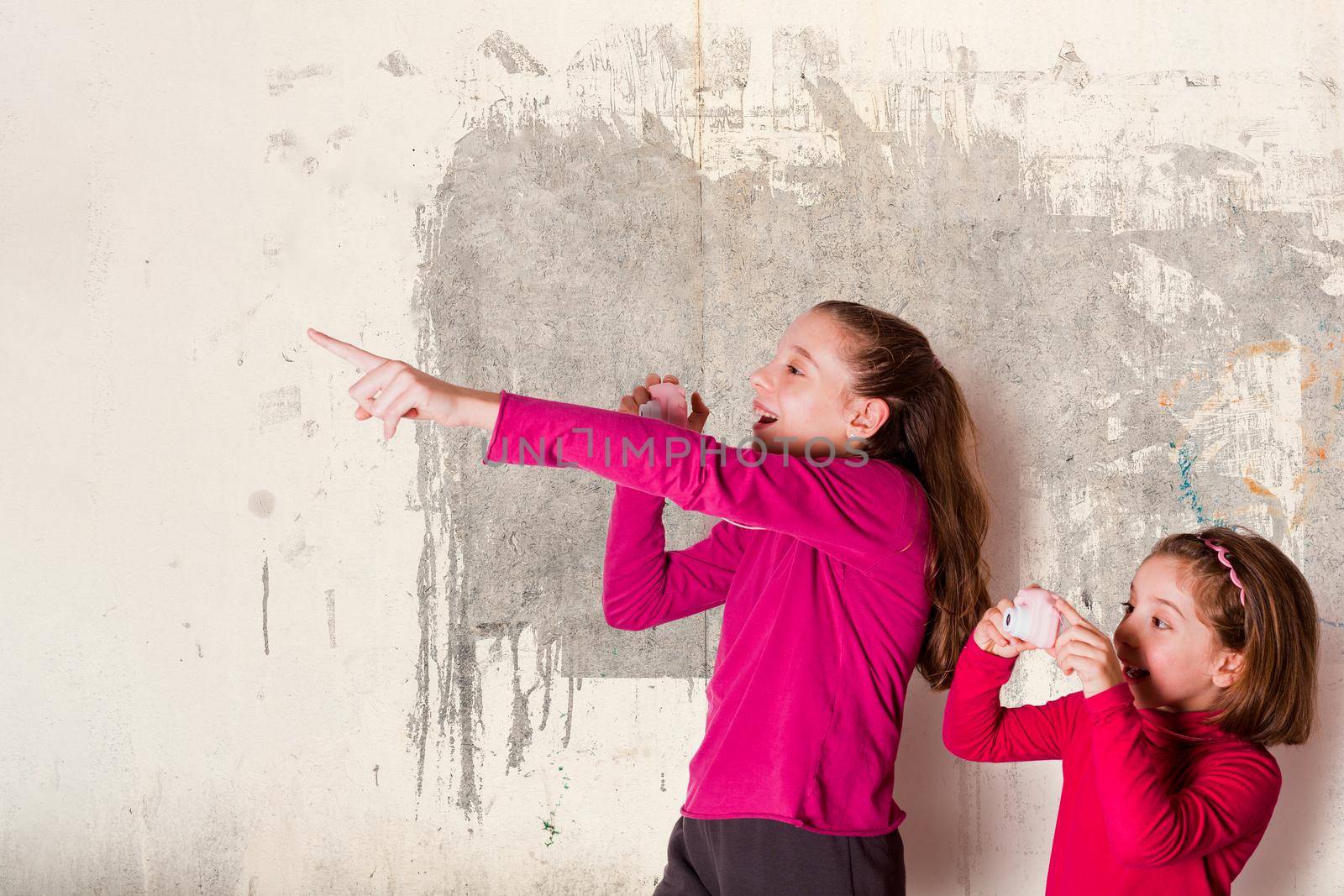 Two Little Girls Taking Picture Using Toy Photo Camera on gray background