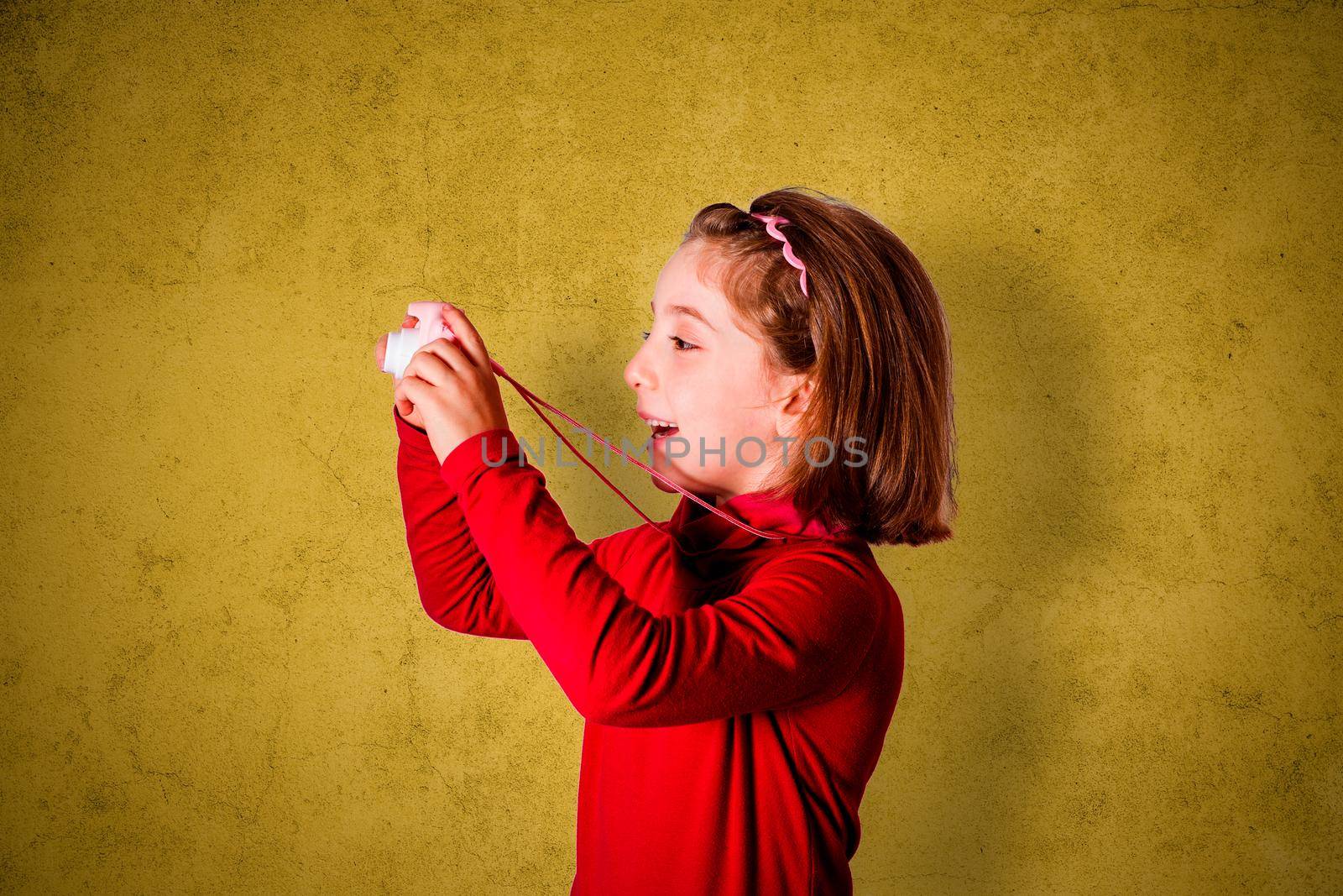 Little Girl Taking Picture Using Toy Photo Camera on yellow background
