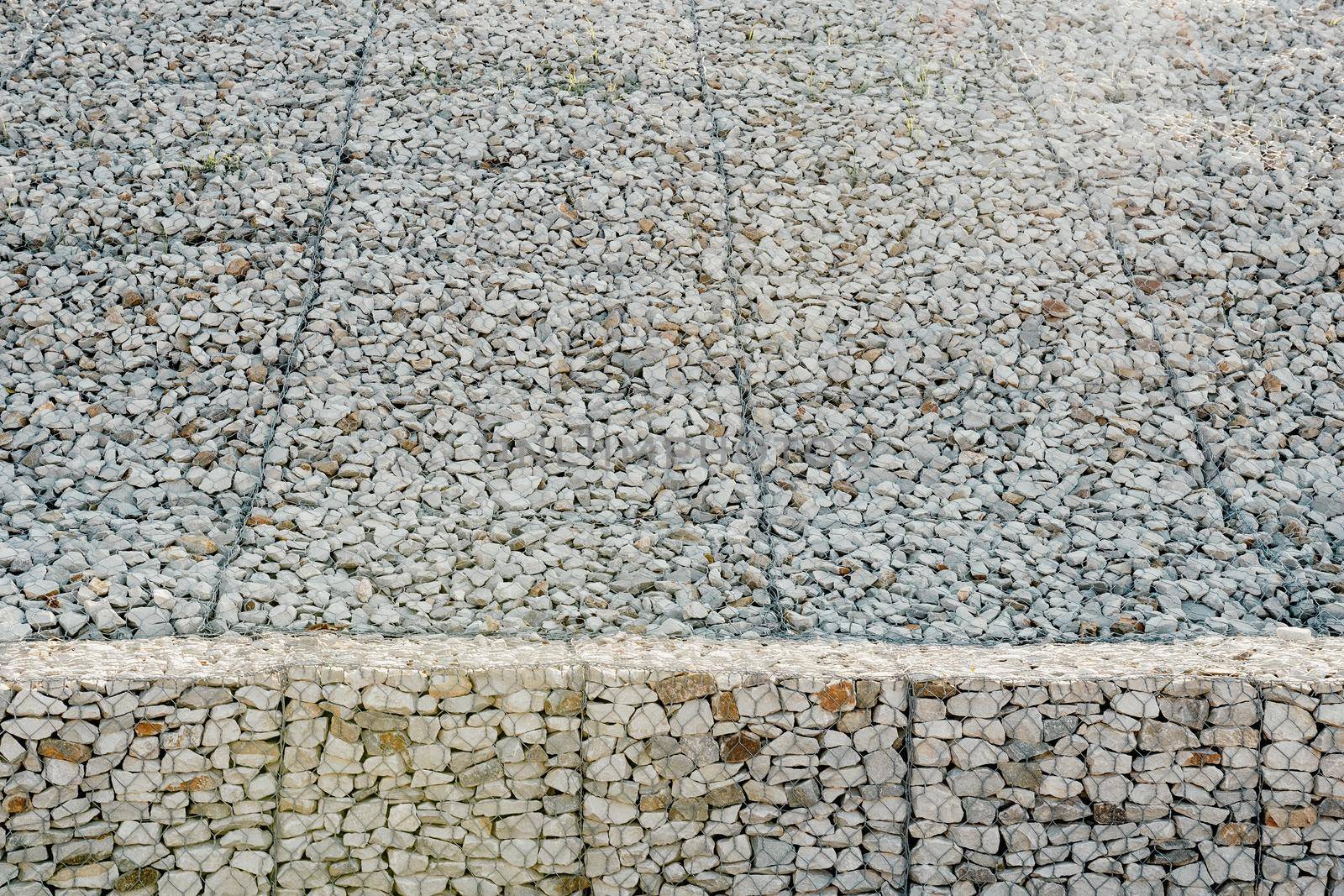 strengthening the slope with stones behind the wire. grey texture. construction. Granite stones behind a metal grate