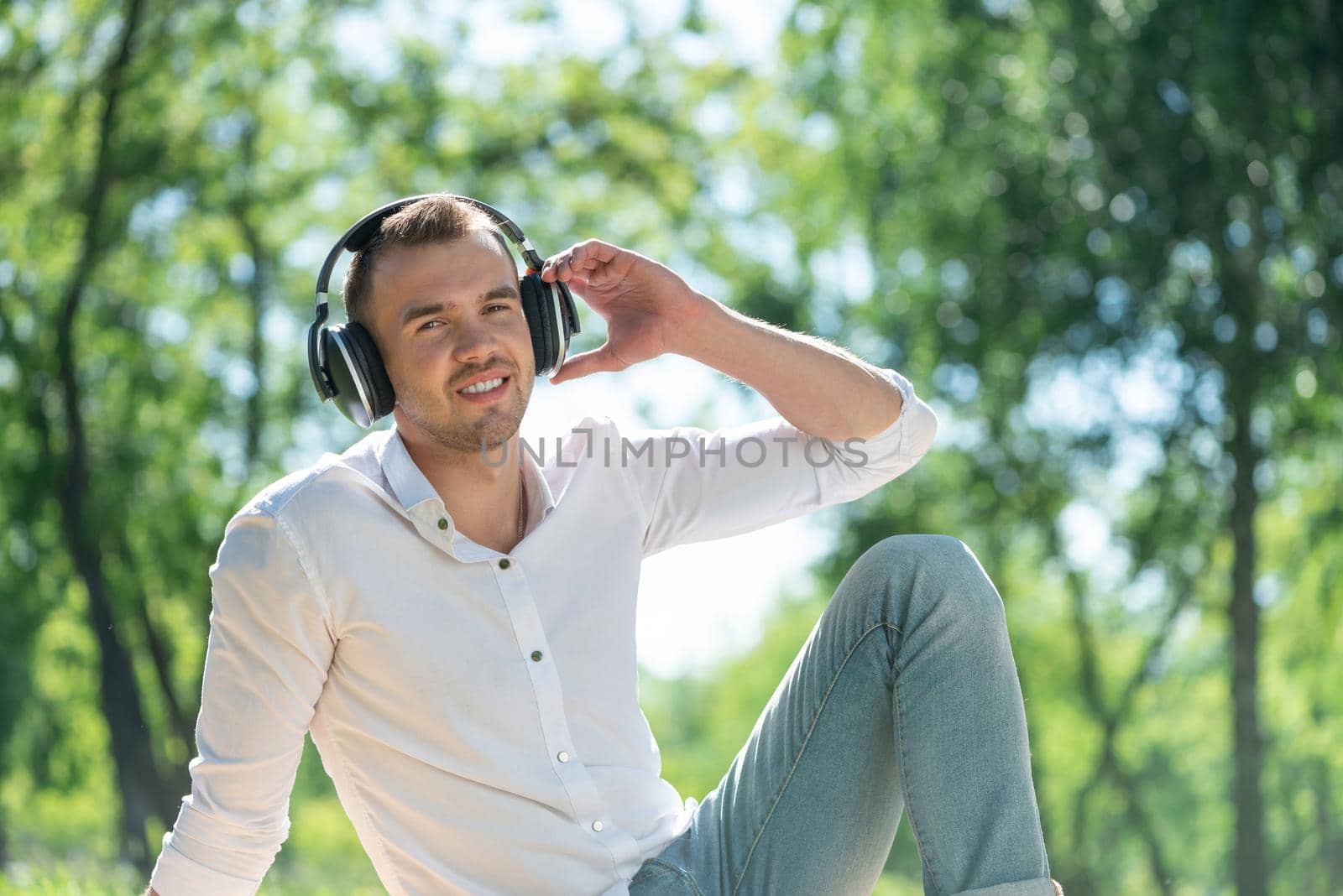 Young man in the park listens to music. He sits on the grass and enjoys music.