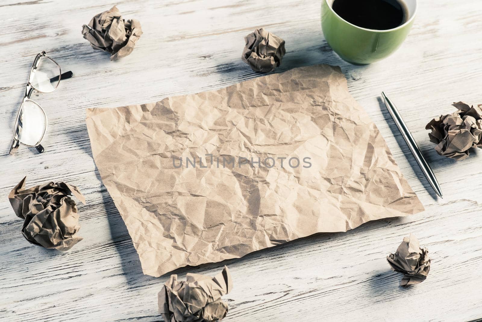 Top view of modern creative workplace with creased piece of sheet, pen, crumpled paper balls and cup of coffee placed on wooden table. Concept of finding of outstanding idea.