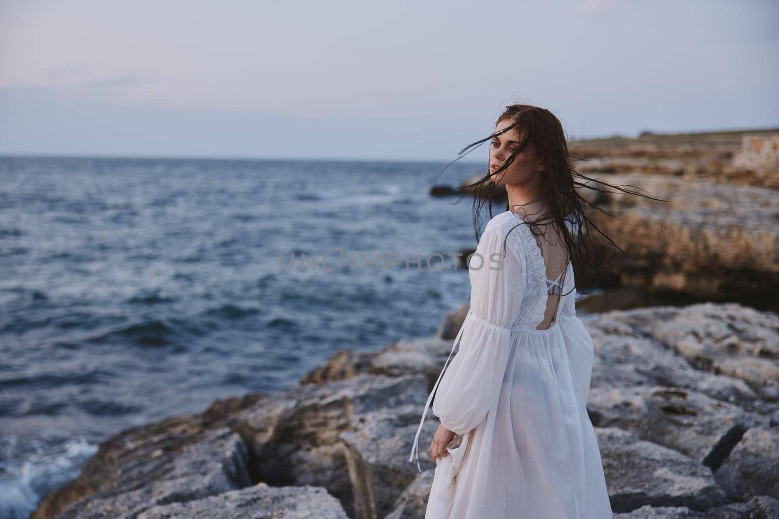 woman with wet hair in a dress on the stony shore of the ocean unaltered. High quality photo