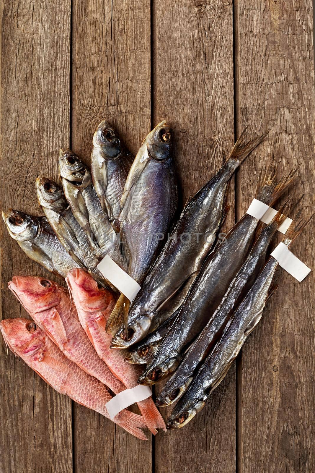 Dried salted roach, sabrefish and red mullets with labels on tails on wooden background by nazarovsergey