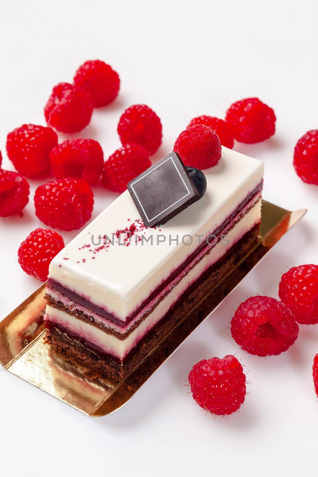 Delicate chocolate sponge cake with light mascarpone cream, sweet jellied raspberry jam, sugar icing on top and fresh ripe berries on white background