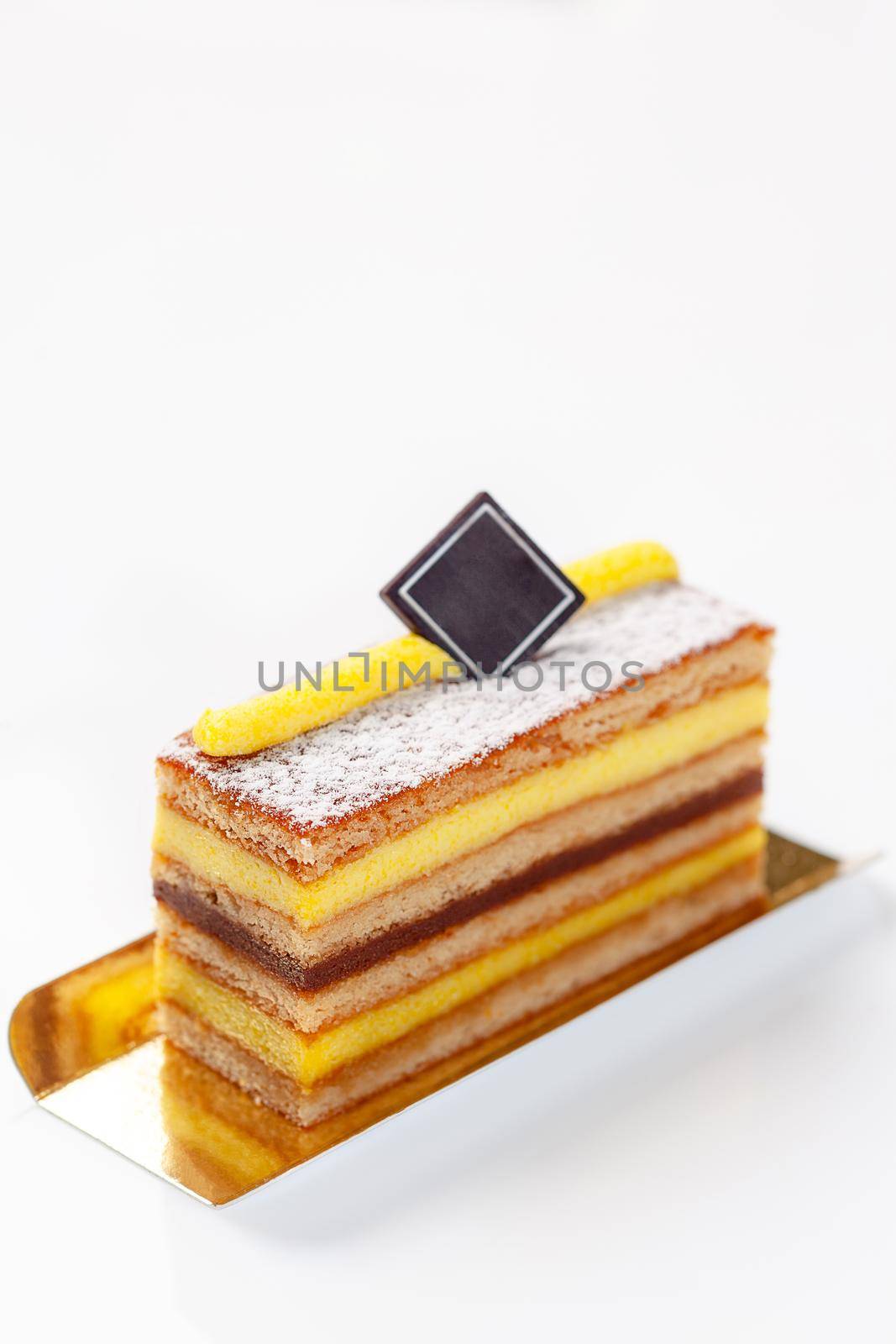 Delicate honey cake slice with mascarpone and caramel cream garnished with powdered sugar and piece of chocolate on white background