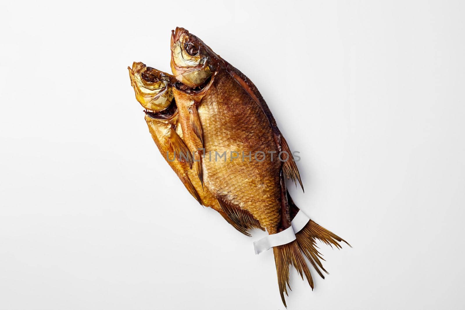 Bunch of two cold smoked breams lying on white surface, top view with copyspace. Paper labels on fish tails for your logo