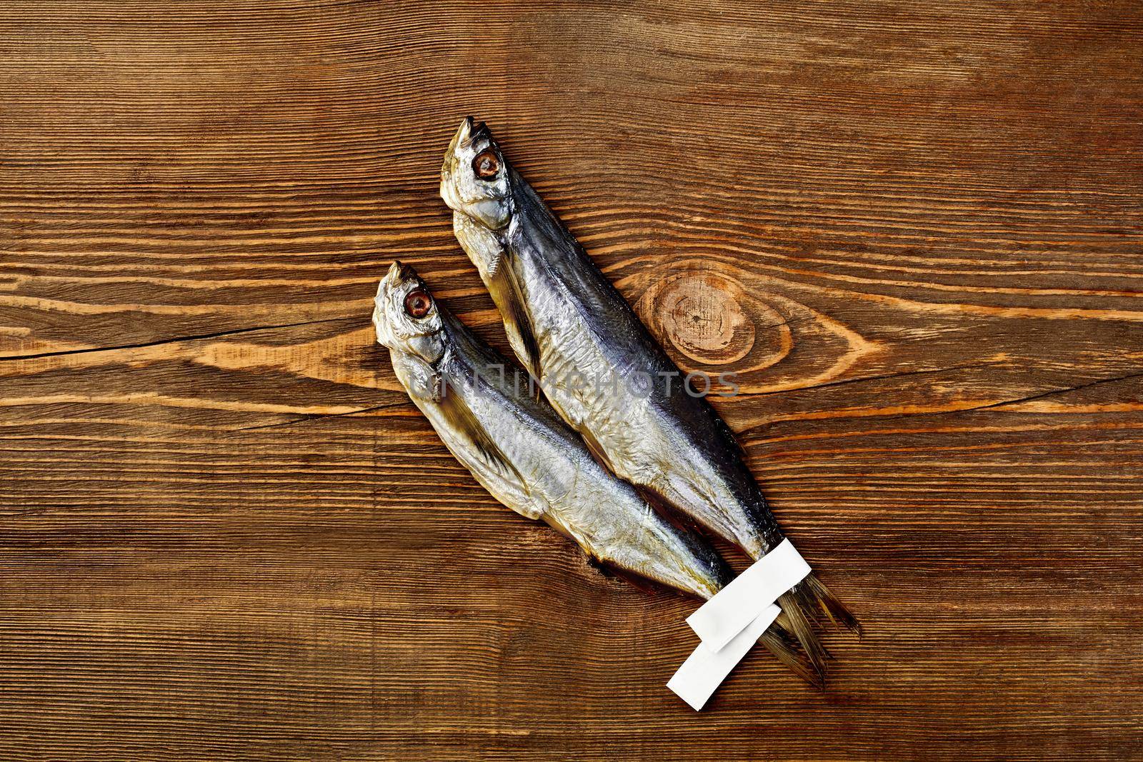 Two salted sun-dried sabrefish with paper labels on tails lying on brown wooden surface, top view with copyspace