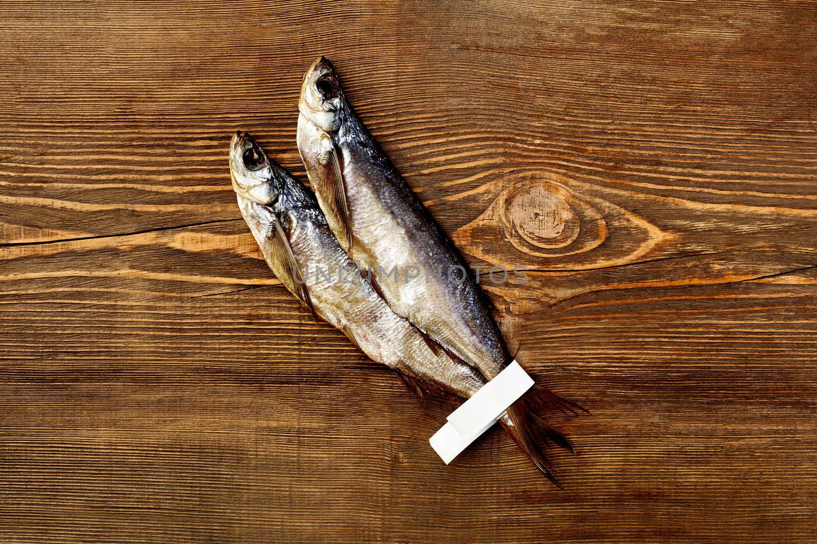 Top view of two salted air-dried sabrefish with paper labels on tails on rustic wooden table background with copyspace. Popular fish appetizer concept