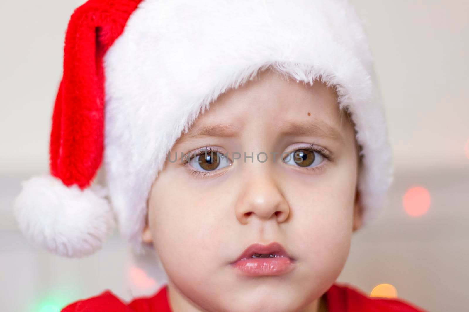 Portrait of a cute boy in a Santa Claus hat. Funny smiling child. Gifts, toys, joy, celebration. Christmas concert.