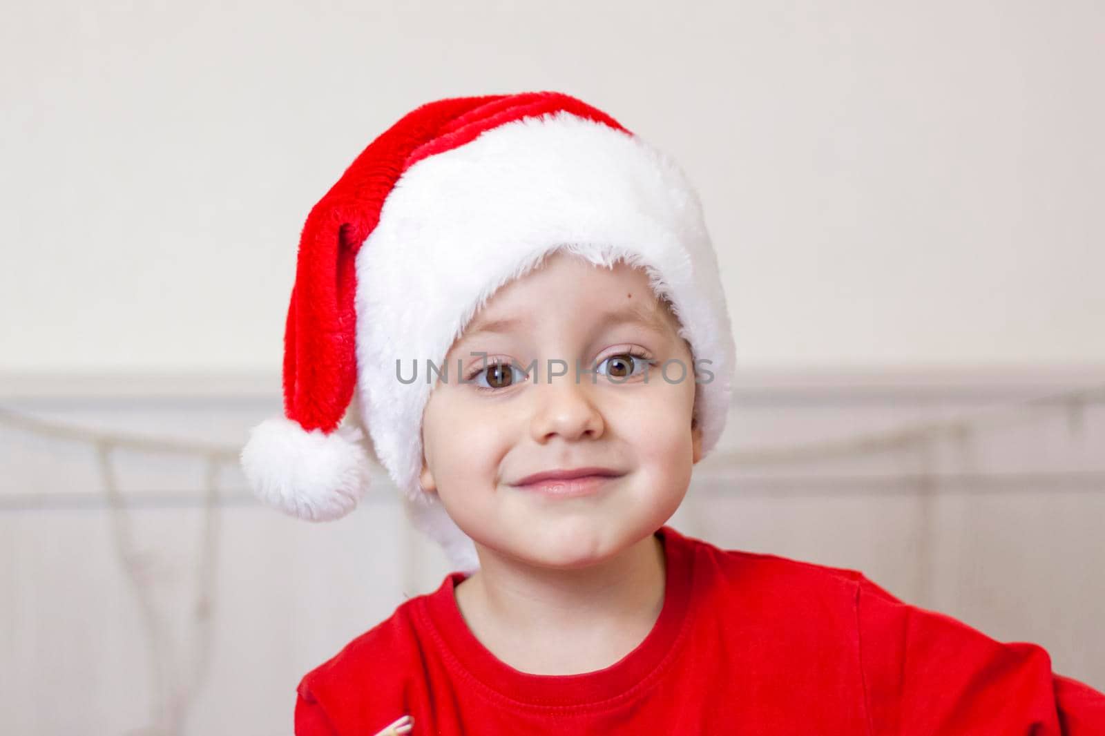 Portrait of a cute boy in a Santa Claus hat. Funny smiling child. Gifts, toys, joy, celebration. Christmas concert.