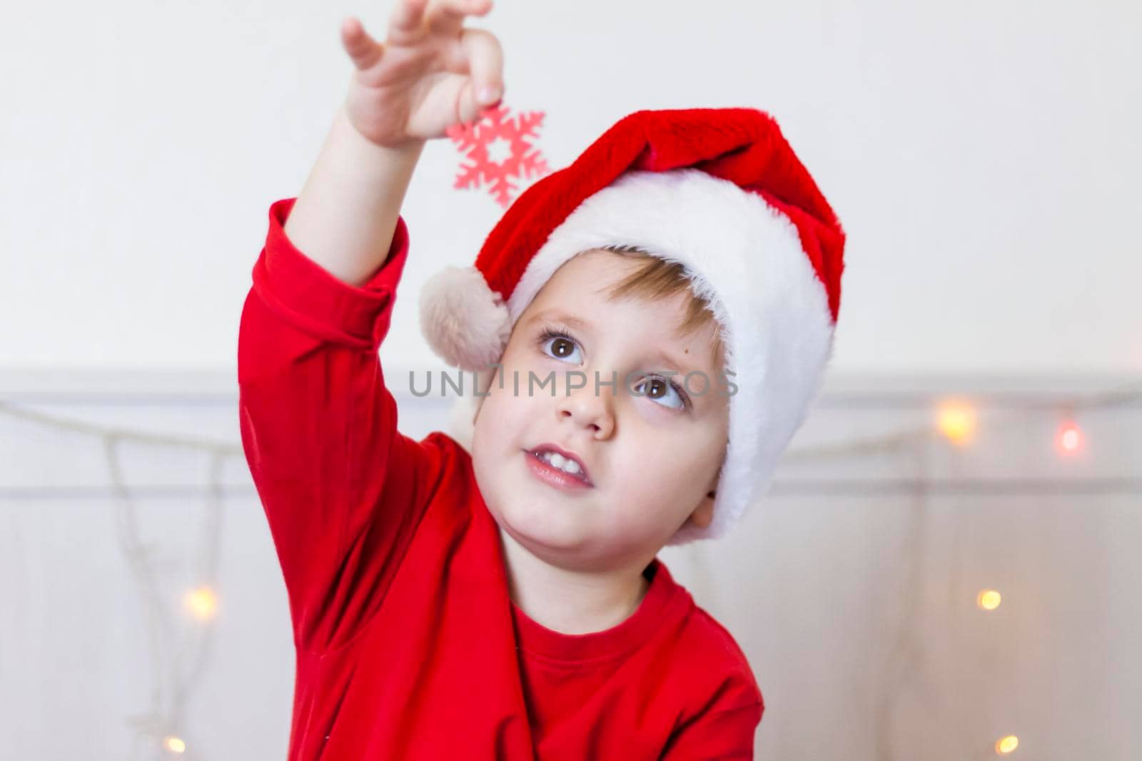 Portrait of a cute boy in a Santa Claus hat. Funny smiling child. Gifts, toys, joy, celebration. Christmas concert.