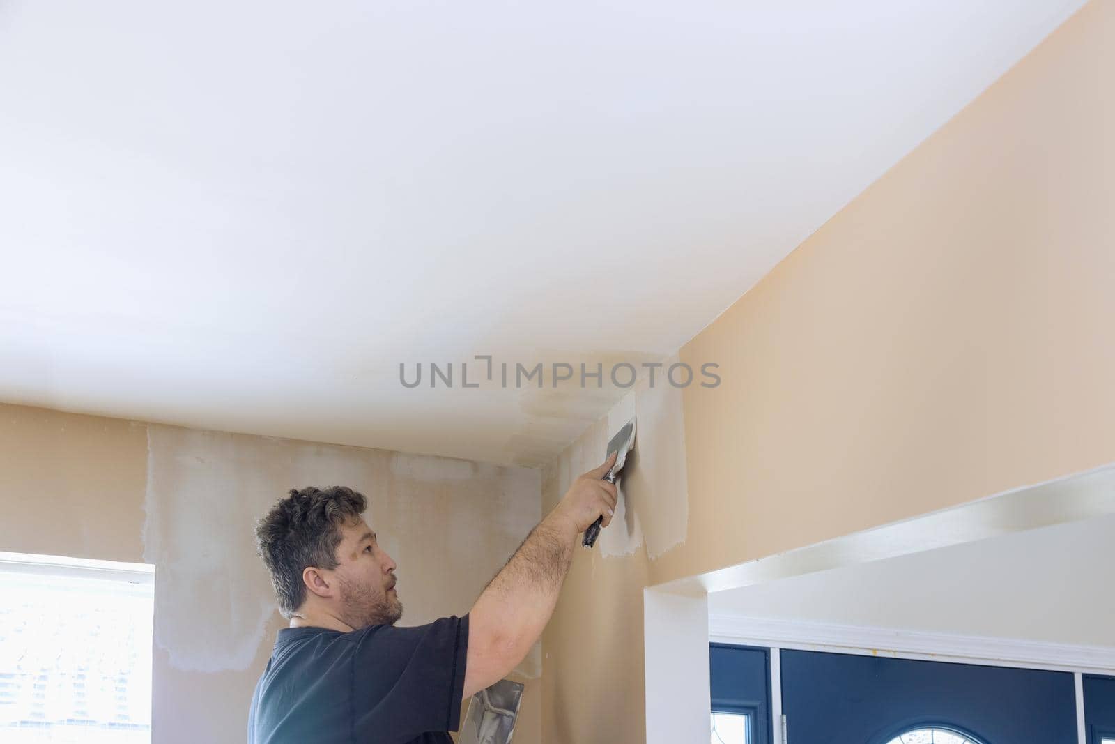 Man putting up a plasterboard a spatula on the white plaster on the wall. by ungvar