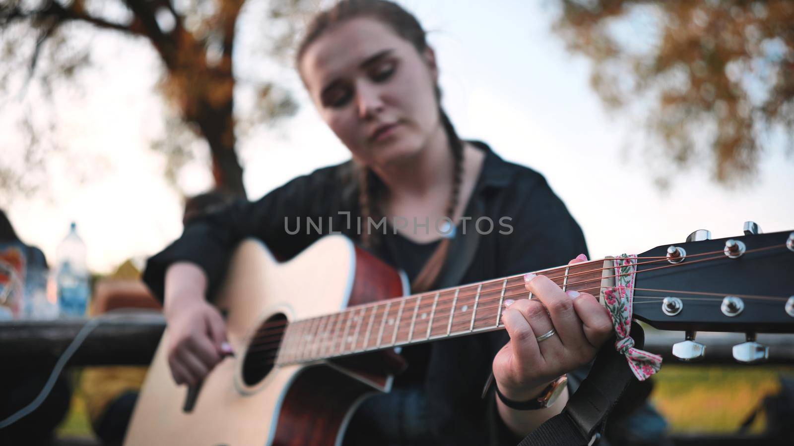 A young girl in nature plays the guitar during a picnic with friends
