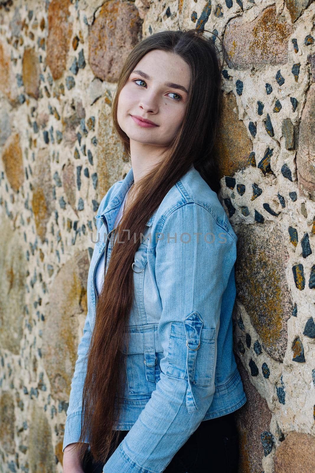 Portrait of a long-haired girl in a denim jacket against a stone wall. by DovidPro
