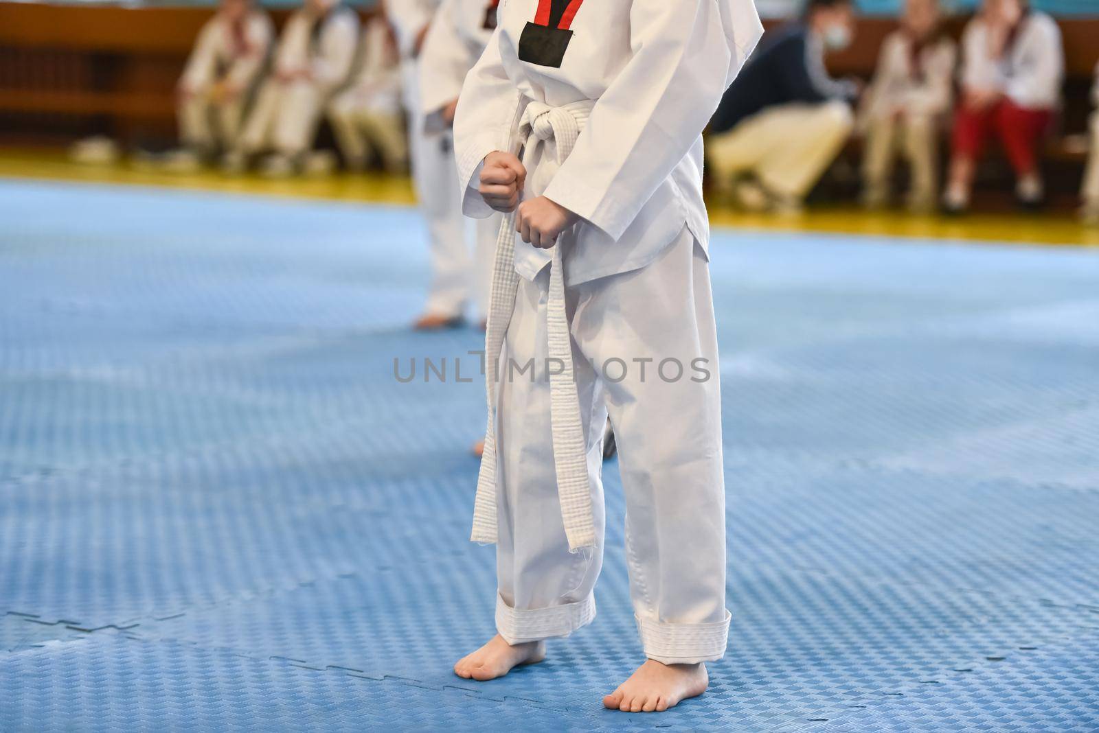 Taekwondo kids. A boy athlete stands in a taekwondo uniform with a white belt during a taekwondo tournament.