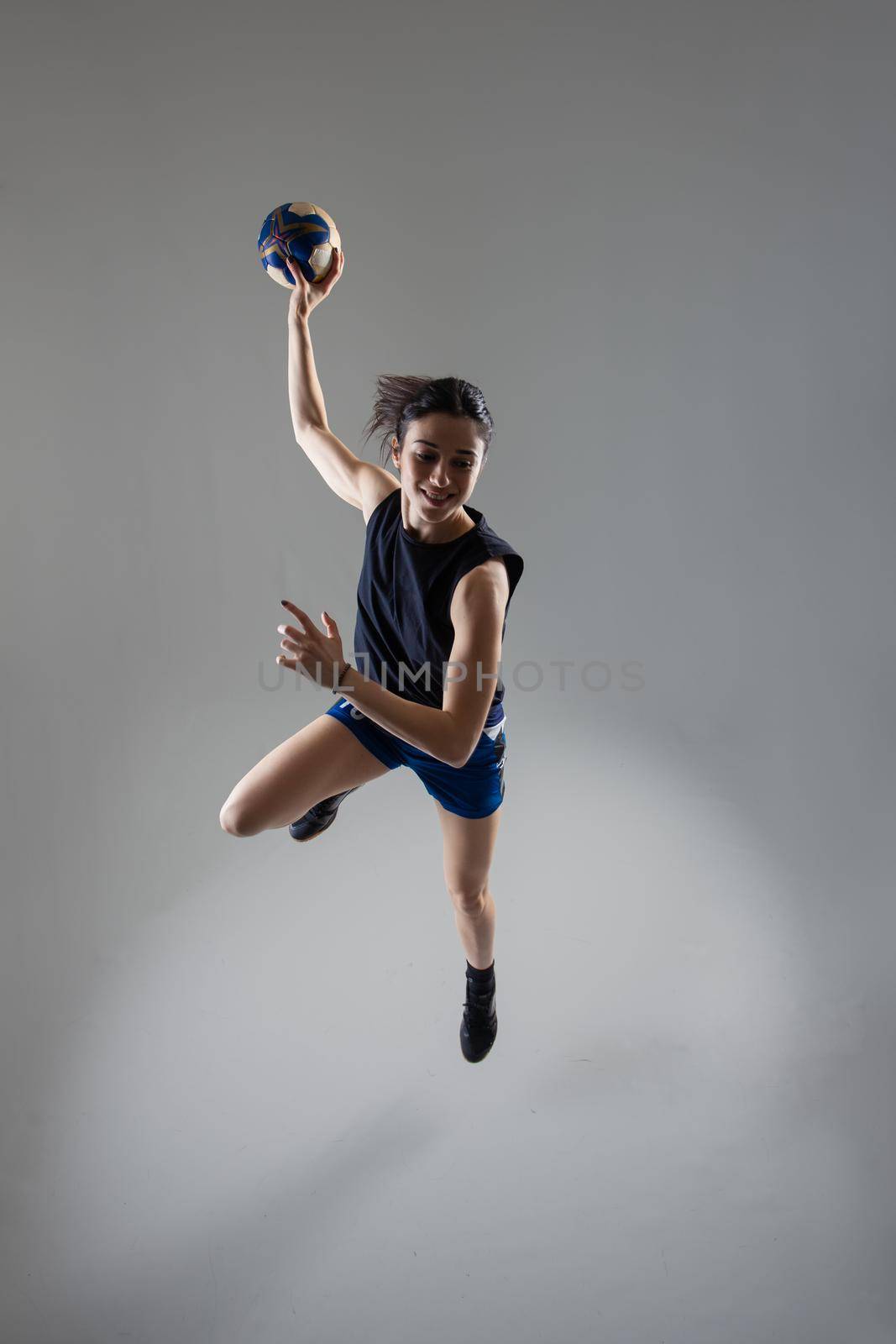 Handball player posing on light gray background. Girl jumping with ball.