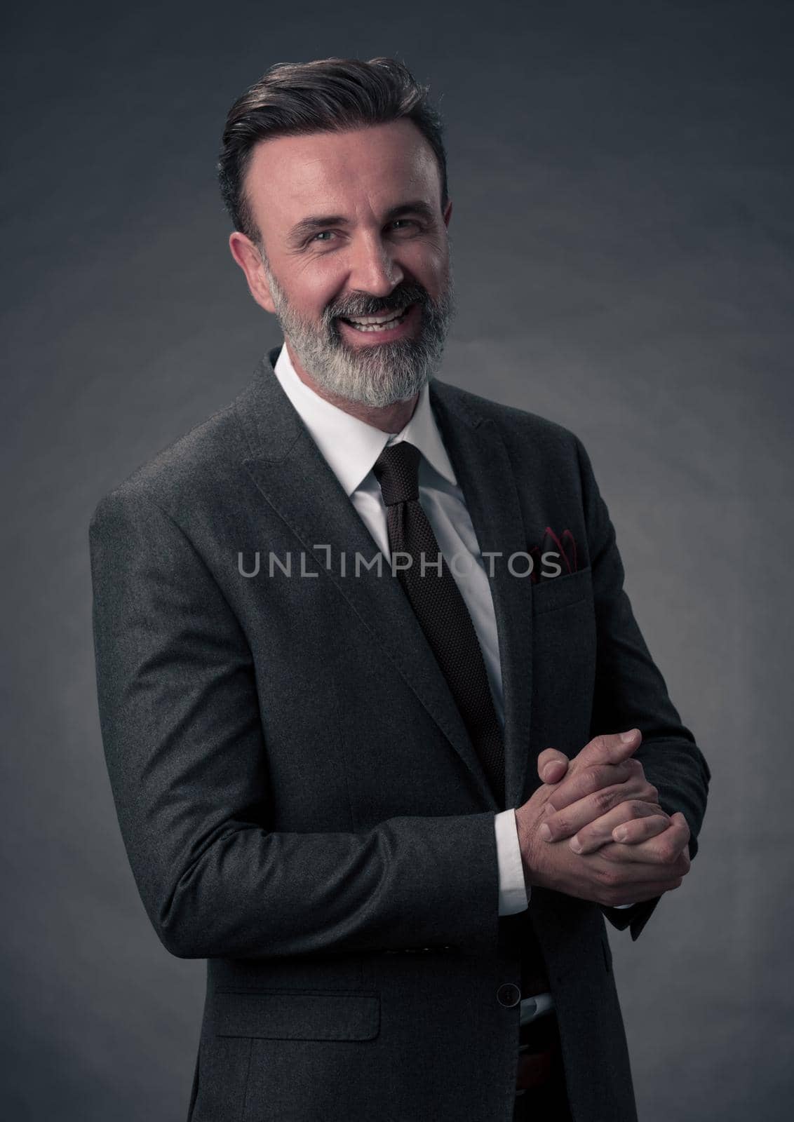 Portrait of a stylish elegant senior businessman with a beard and casual business clothes in photo studio isolated on dark background gesturing with hands by dotshock