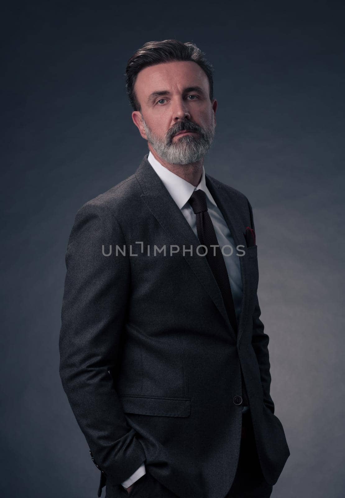 Portrait of a successful stylish elegant senior businessman with a grey beard and casual business clothes confident in photo studio isolated on dark background gesturing with hands. High-quality photo