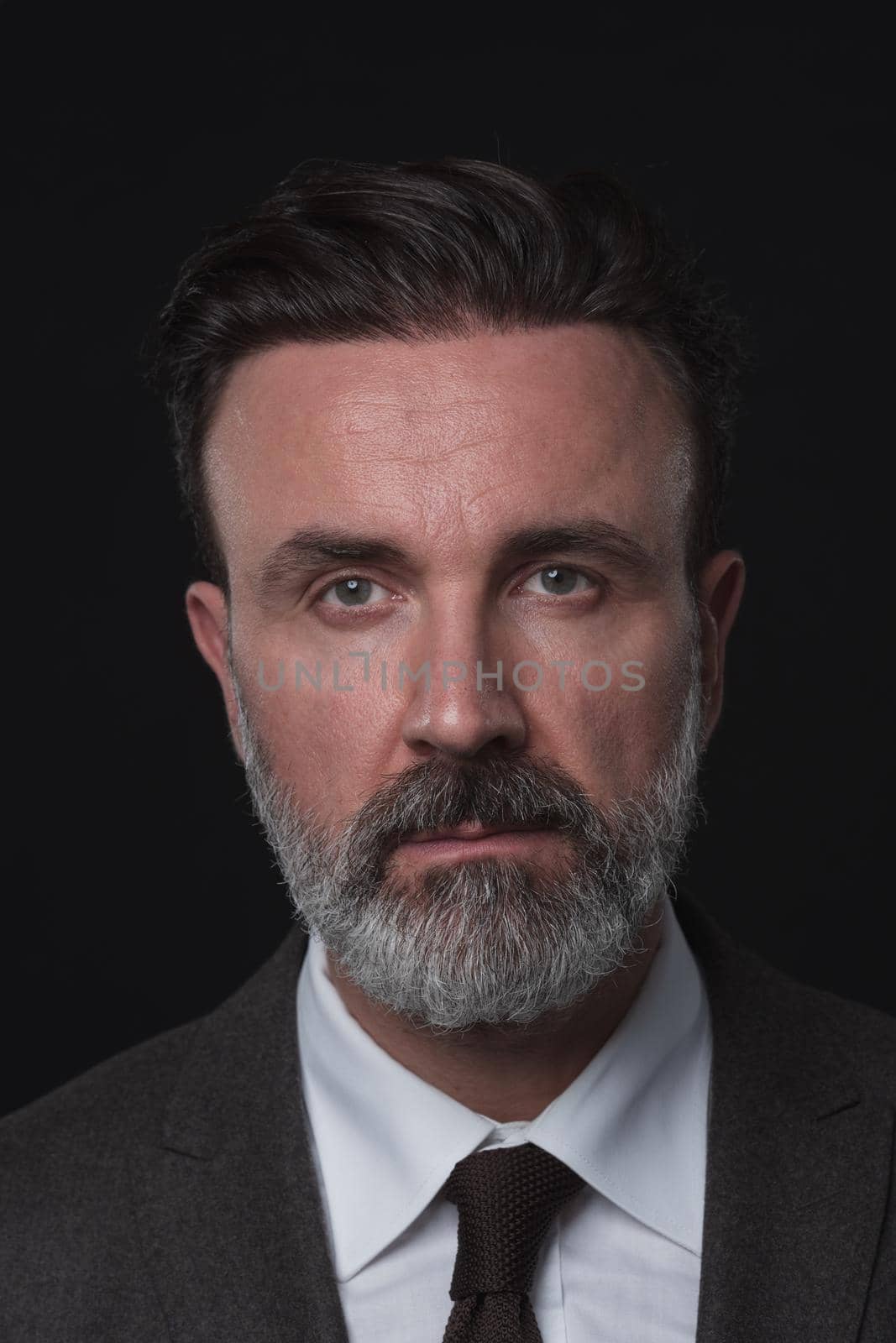 Portrait of a successful stylish elegant senior businessman with a grey beard and casual business clothes confident in photo studio isolated on dark background gesturing with hands. High-quality photo