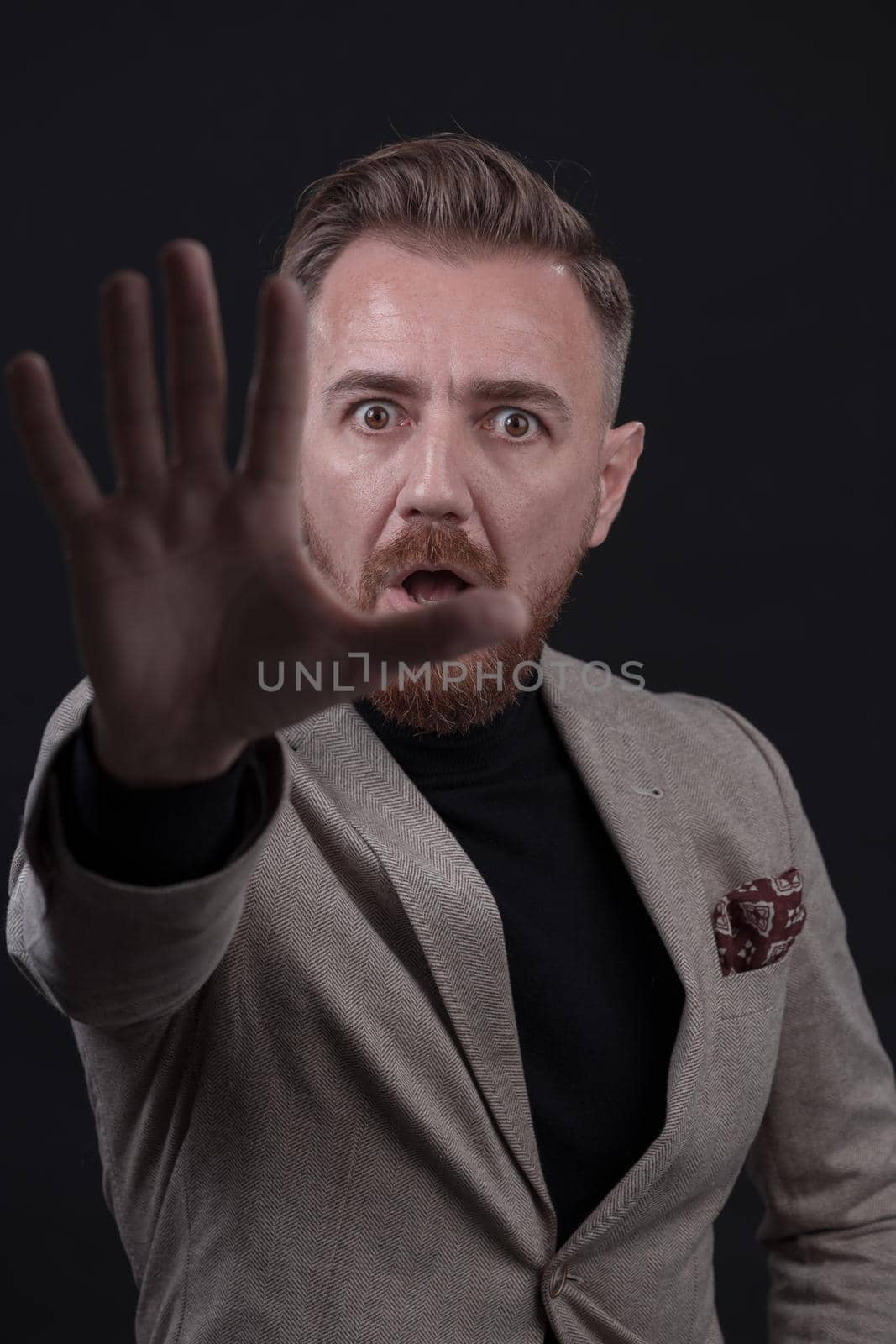 Portrait of a stylish elegant senior businessman with a beard and casual business clothes in photo studio isolated on dark background gesturing with hands. High quality photo