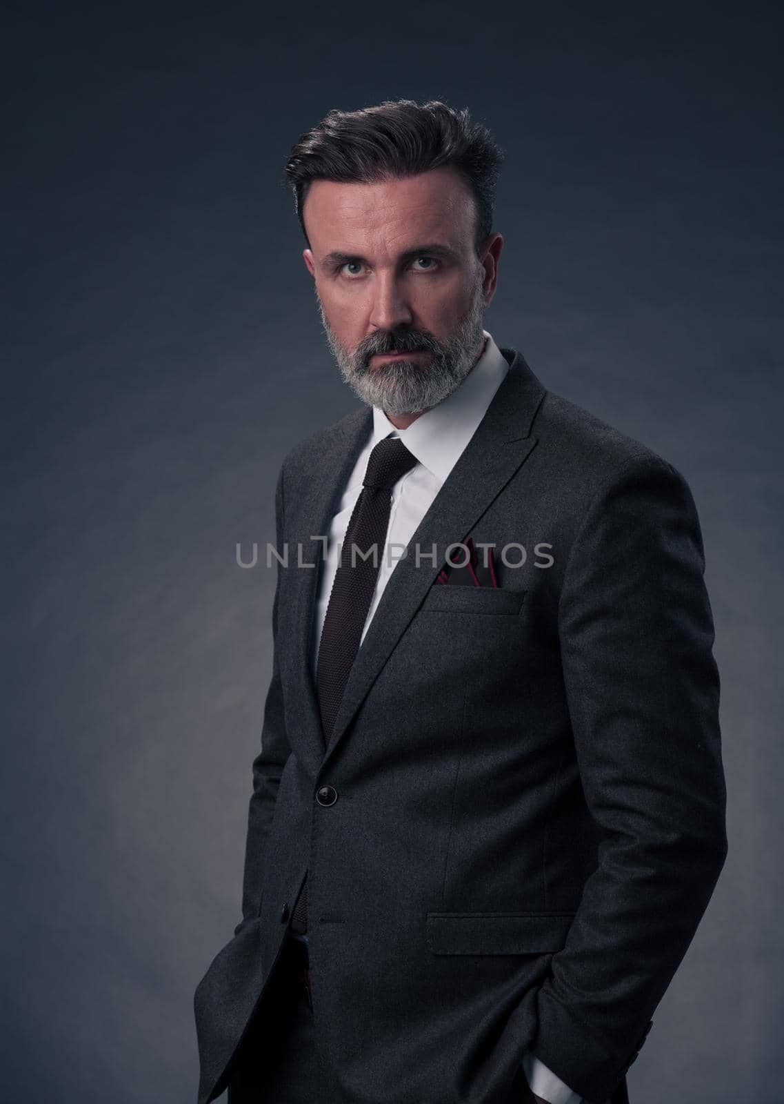 Portrait of a stylish elegant senior businessman with a beard and casual business clothes in photo studio isolated on dark background gesturing with hands by dotshock