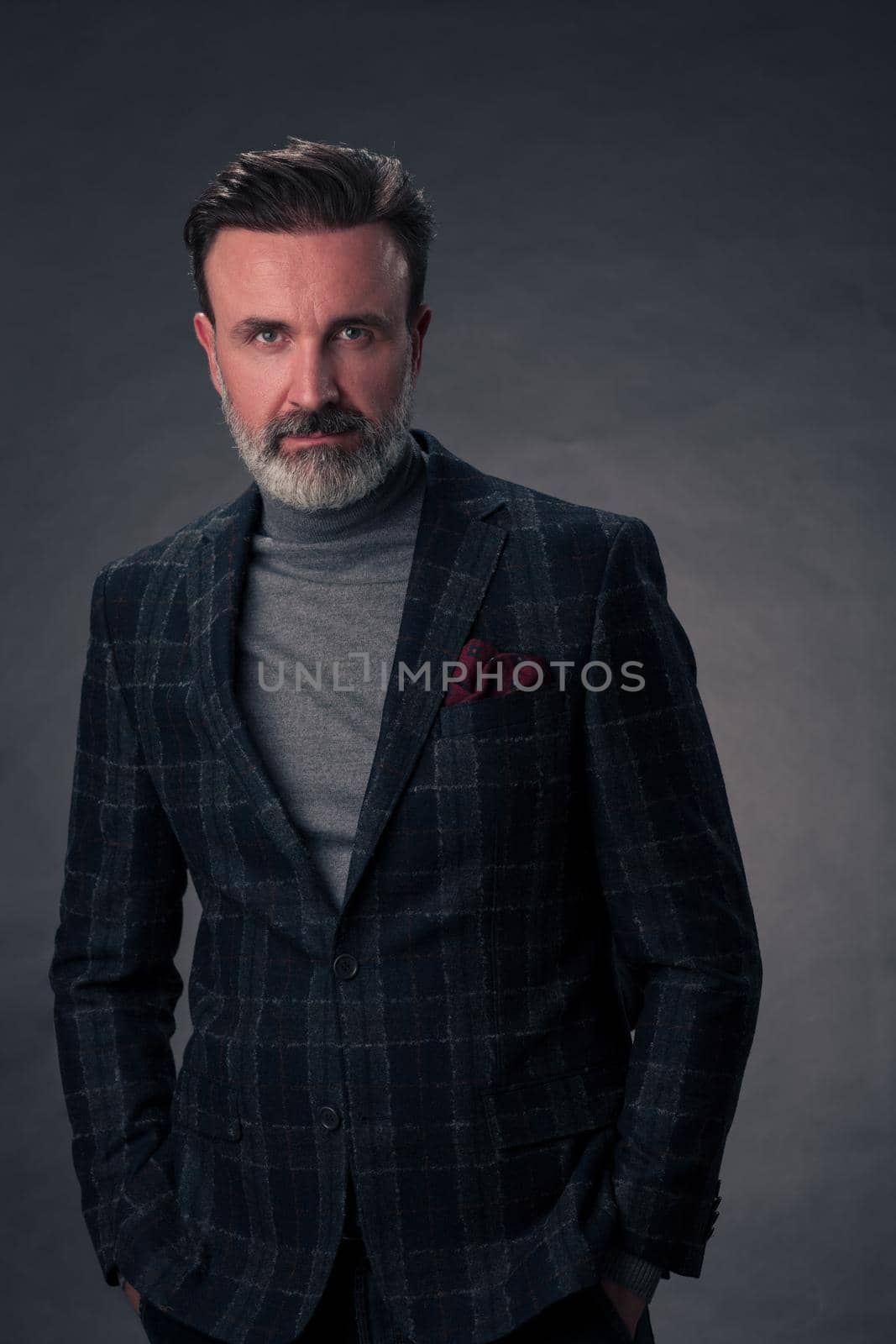 Portrait of a successful stylish elegant senior businessman with a grey beard and casual business clothes confident in photo studio isolated on dark background gesturing with hands. High-quality photo