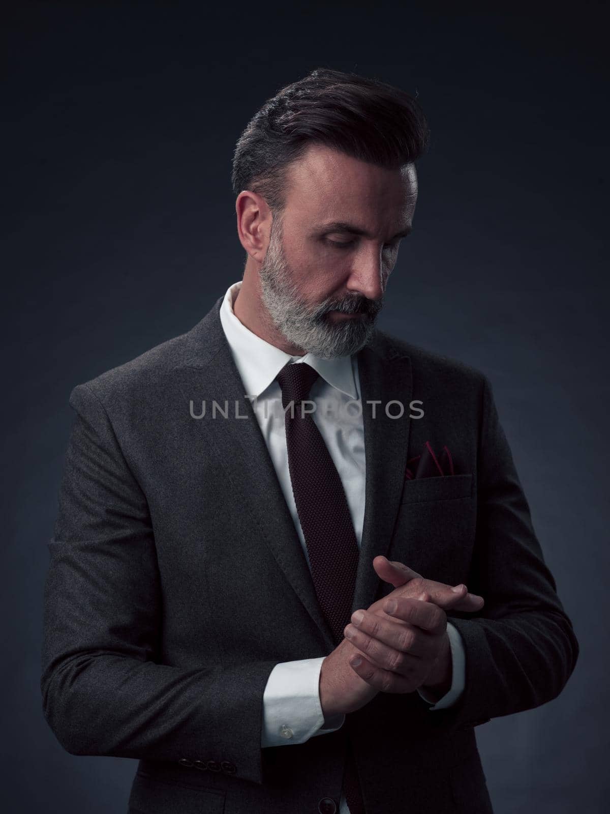 Portrait of a successful stylish elegant senior businessman with a grey beard and casual business clothes confident in photo studio isolated on dark background gesturing with hands. High-quality photo