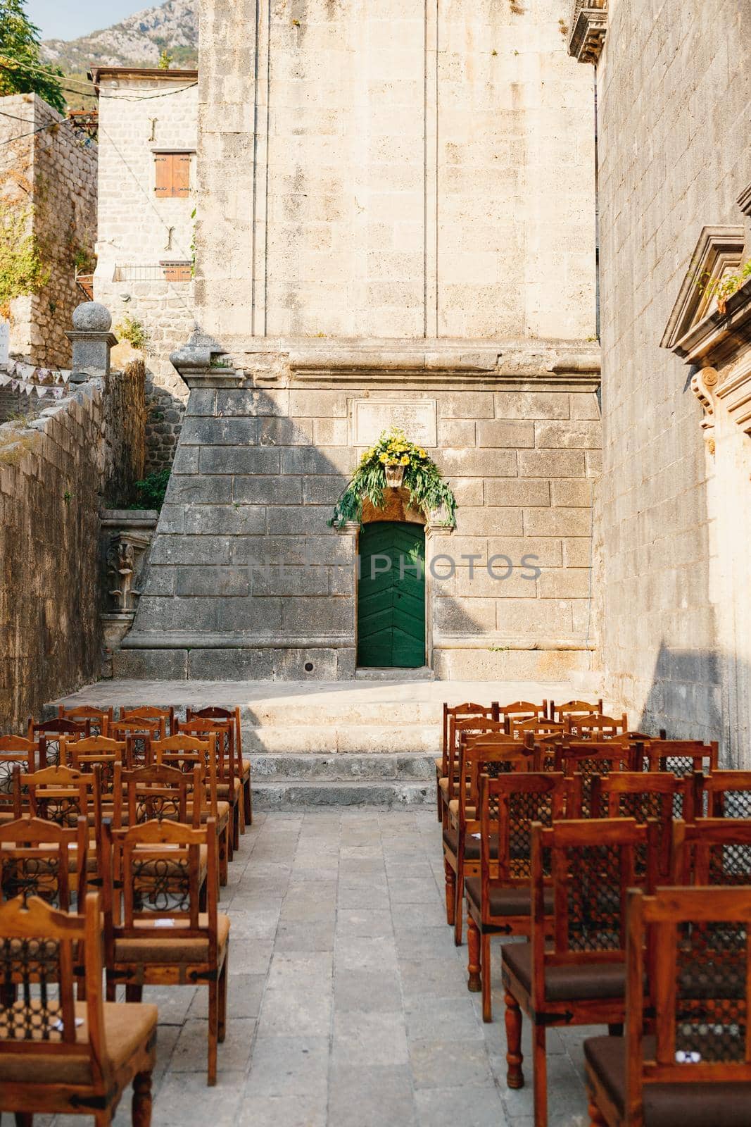 Wooden chairs with patterns on the backs stand in rows on the cobblestones in front of the church door. High quality photo